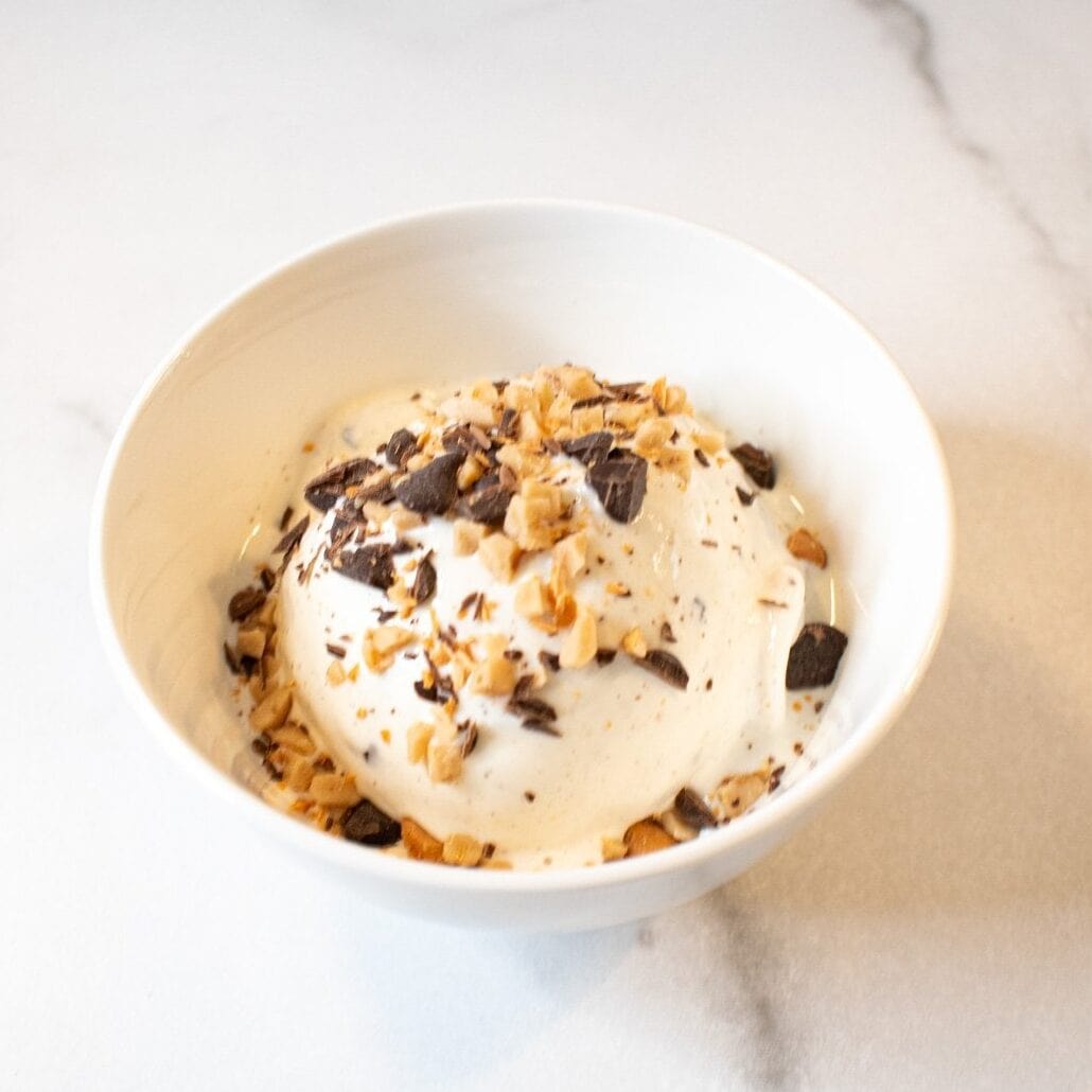 Cookies and cream ice cream with chocolate chunks and crushed cookies in a white bowl.